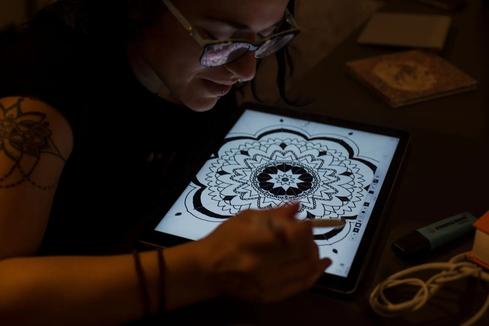 A digital artist uses a tablet for creative mandala design work in a dimly lit setting.